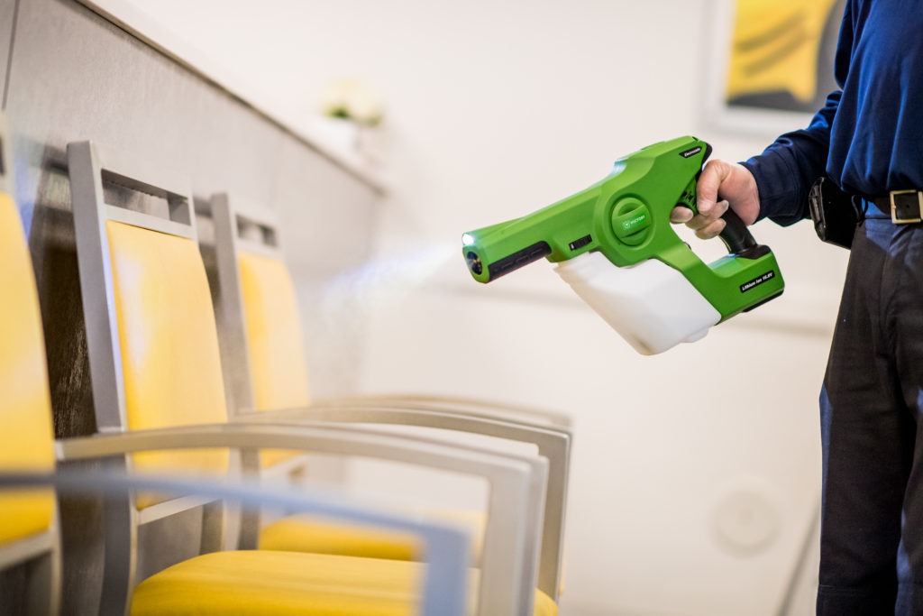 HCDG employee using a disinfecting sprayer on chairs in a facility lobby.