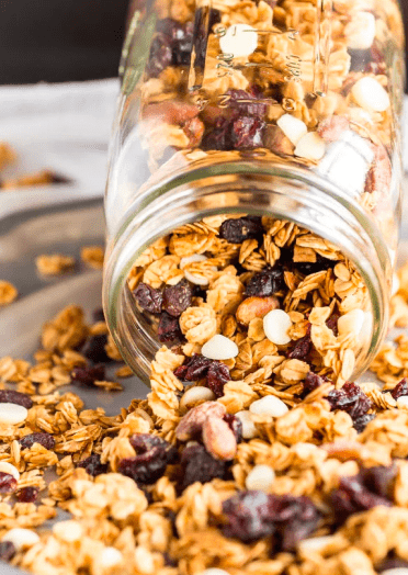 A mixture of oats, raisins, and white chocolate chips being poured out of a mason jar on to a plate.