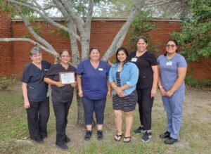 Group of six HCSG employees standing outside with one holding an award.