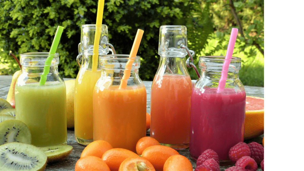 Five rainbow-colored smoothies sitting on a wooden lawn table with assorted fruit in the foreground.