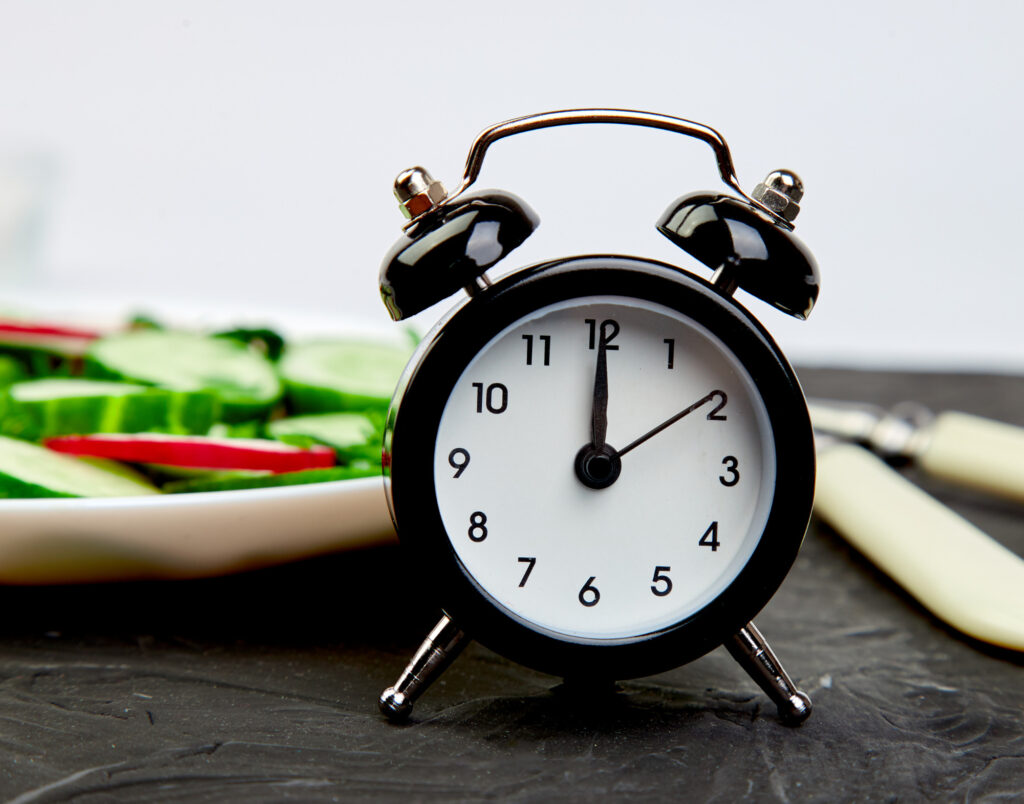 Clock in foreground with plate of vegetables in the background.