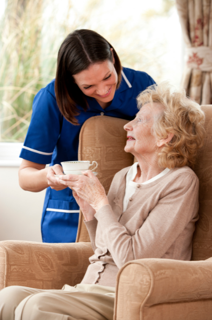 Image of HCSG staff dining staff smiling with account management. Dining staff member serving tea to a facility resident sitting in a wingback chair.