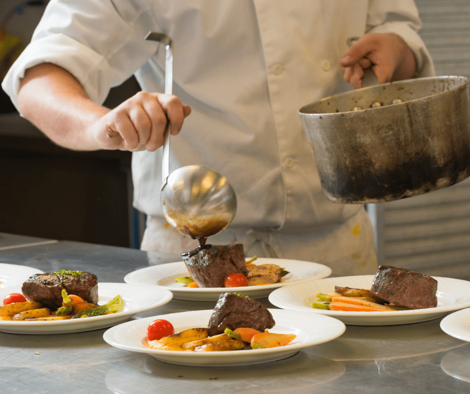 An image of a chef pouring sauce atop a steak filet accompanied by vegetables.
