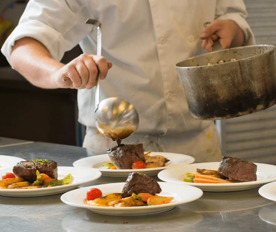 An image of a chef pouring sauce atop a steak filet accompanied by vegetables.