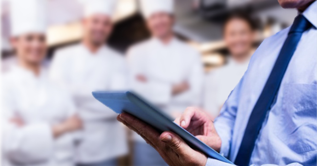 A man in a suit reviewing a checklist in front four people dressed in chef uniforms
