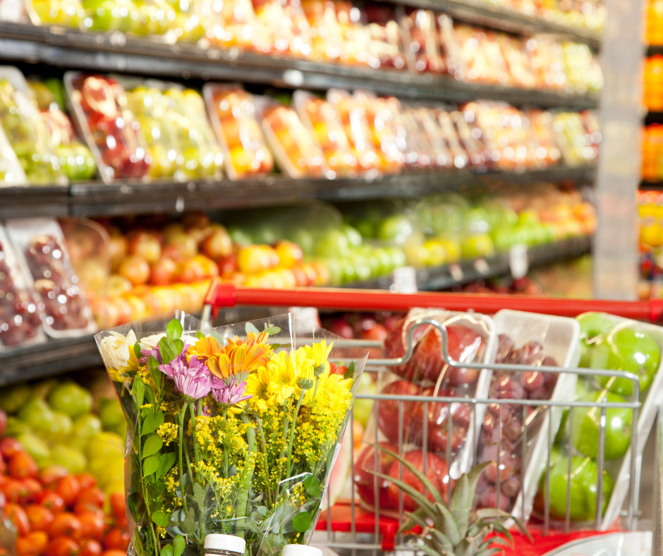 image of a cart filled with fruits and veggies in the foreground and an aisle of fruits and veggies blurred in the background