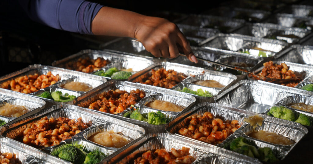 Woman serving pasta into containers at volunteer event.