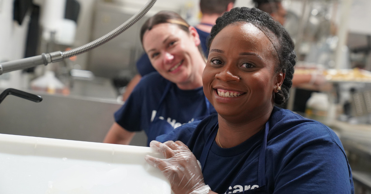 Two HCSG volunteers smiling at the camera while washing dishes.