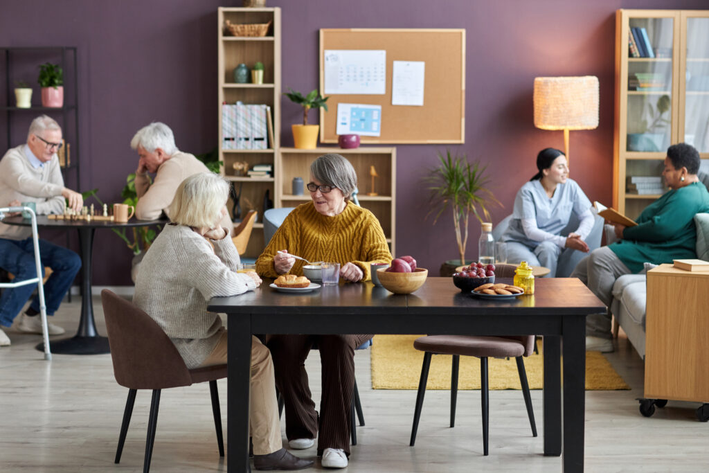 Full length view at common room in retirement home with diverse group of seniors enjoying leisure activities.