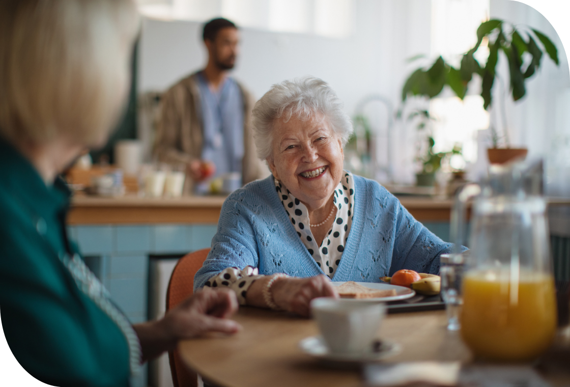Smiling caregiver warmly interacts with a senior woman in a healthcare setting. Compassionate care and positive engagement in a senior living community.