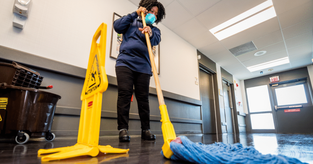An HCSG employee mops the floor while a yellow wet floor sign is placed in front of her.
